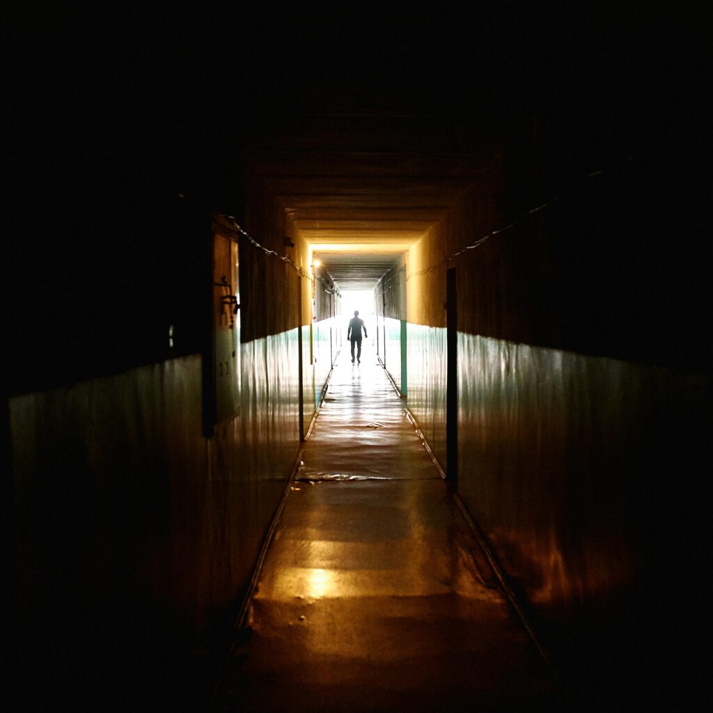 A silhouette of a person walking through a dimly lit corridor with dramatic light and shadows.